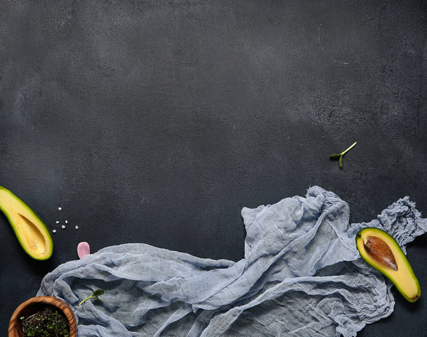 Half of avocado with blue cloth. Dark textured slate background. Rustic keto diet concept.  - Zdjęcie, obraz