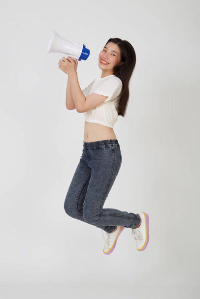Piękna młoda kobieta skacze z megafonem na białym studio - Zdjęcie, obraz