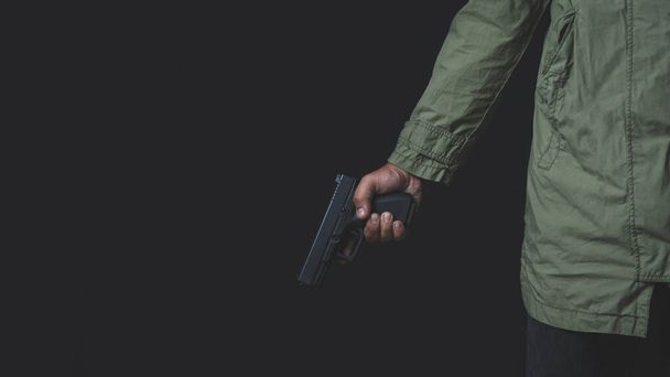 Man holding a gun in his hand with a black background, rearview. Man with a pistol in his hand aims his target. - Foto, immagini