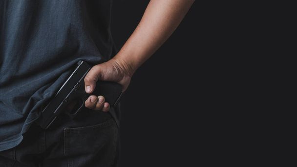Man holding a gun in his hand with a black background, rearview. Man with a pistol in his hand aims his target. - Photo, Image