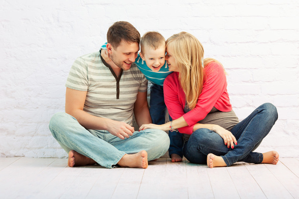 Familia feliz de tres sentados en el suelo cerca de la pared y riendo: madre, padre y niño pequeño. Mamá está embarazada.
. - Foto, imagen