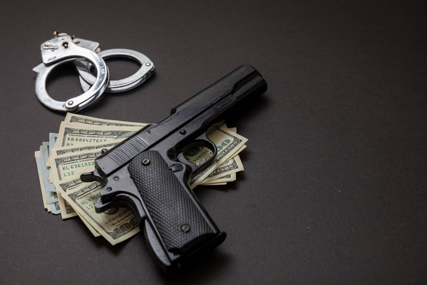 Koncept zločinu a práva. Pistolová pistole 9 mm, pouta na ruce a americké dolarové bankovky na černém pozadí. Trestní peníze a trest, kopírovací prostor, šablona - Fotografie, Obrázek