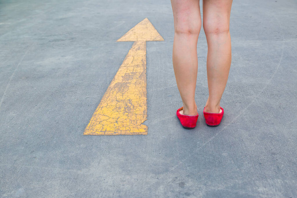 Mädchen trägt rote Schuhe, die auf einer asphaltierten Straße mit gelbem Verkehrszeichen auf sie zugehen - Foto, Bild