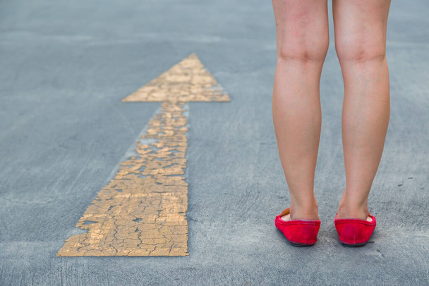 Lány piros cipőt visel felé sétál sárga közlekedési nyíl felirat aszfalt út háttér - Fotó, kép