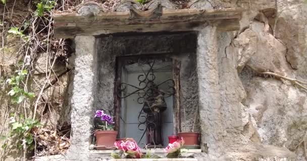 Vallásos szobor kőfali résben. Utcai szent oltár hagyományos katolikus alakkal. Vallásos keresztény szimbólumok az ablakban. - Felvétel, videó