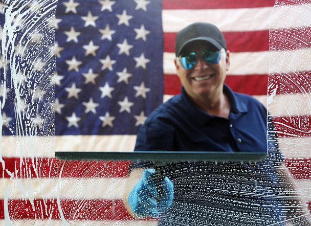 Window Cleaning. Window Washing. American Window Washing. American Window Washing. Professional Window Cleaner. Window Cleaning. Window Washing. American flag background.  A window washer cleans windows with his squeegee and soapy water. Clean Glass. - Photo, Image