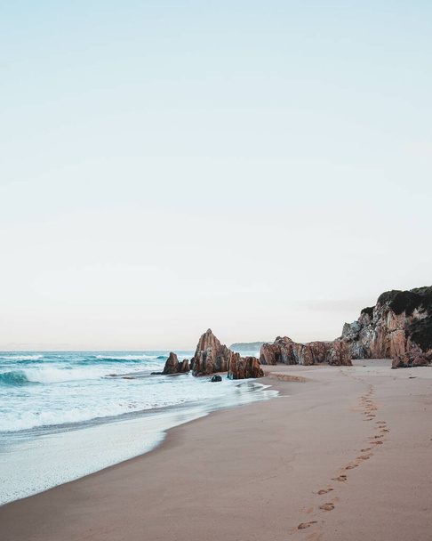 A vertical shot of an idyllic sandy shore among cliffs - 写真・画像