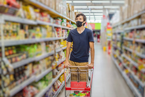 Alarmed man wears medical mask against coronavirus while grocery shopping in supermarket or store- health, safety and pandemic concept - young woman wearing protective mask and stockpiling food - Φωτογραφία, εικόνα