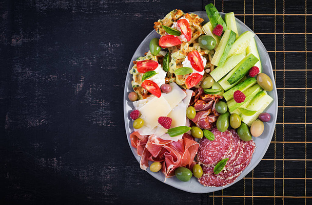 Charcuterie board. Platter: parmesan with prosciutto, salami, cucumbers and olives. Assortment of tasty appetizers or antipasti. Top view, copy space, flat lay - Φωτογραφία, εικόνα