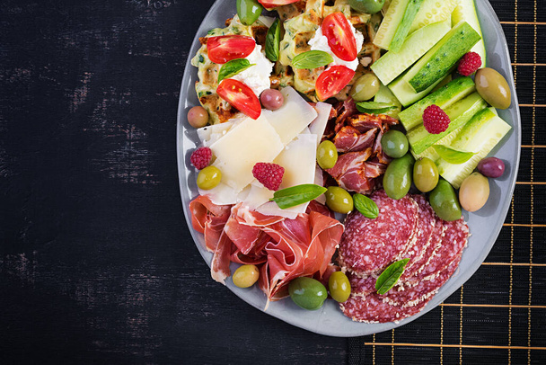 Charcuterie board. Platter: parmesan with prosciutto, salami, cucumbers and olives. Assortment of tasty appetizers or antipasti. Top view, copy space, flat lay - Photo, Image