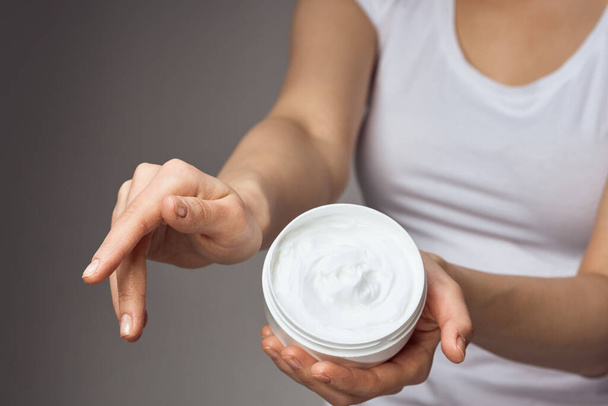 mujer en camiseta blanca sostiene crema en las manos cuidado de la piel hidratante higiene de la salud - Foto, Imagen