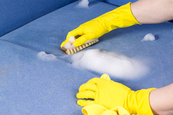 hand in a rubber glove dry cleaning upholstered furniture with a brush, close-up, side view - Foto, Imagem