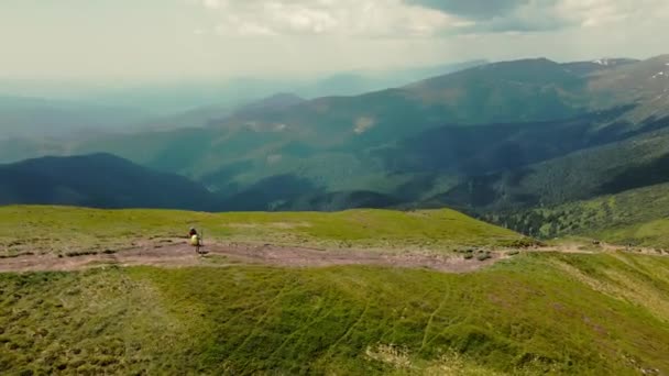 Dva turisté stojící na vrcholu hory s velkými batohy. Extrémně krásné pozadí za nimi. Letecký pohled. Malebná krása kolem okolních hor - Záběry, video