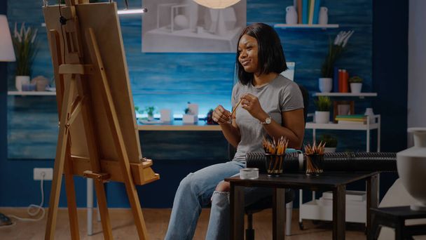 Mulher artista preto sentado no estúdio com tela e cavalete - Foto, Imagem