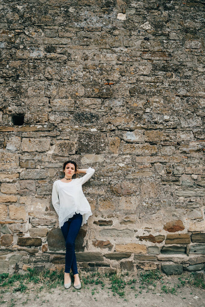 portrait of traveler girl in white dress stands at ancient stone wall - Φωτογραφία, εικόνα