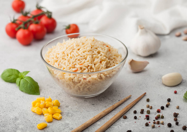 Glass bowl with boiled long grain basmati rice with vegetables on light background with sticks and tomatoes with corn, garlic and basil. - 写真・画像