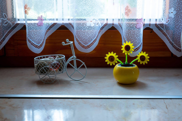 View on a solar powered plastic sunflower moving by the sunlight representing renewable energy source in the window. - Фото, изображение