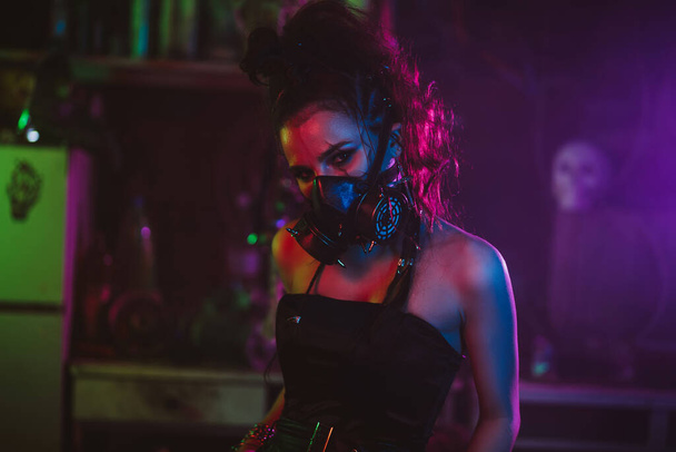 Cyberpunkowy cosplay. Dziewczyna w masce gazowej w postapokaliptycznym stylu z neonowym oświetleniem - Zdjęcie, obraz
