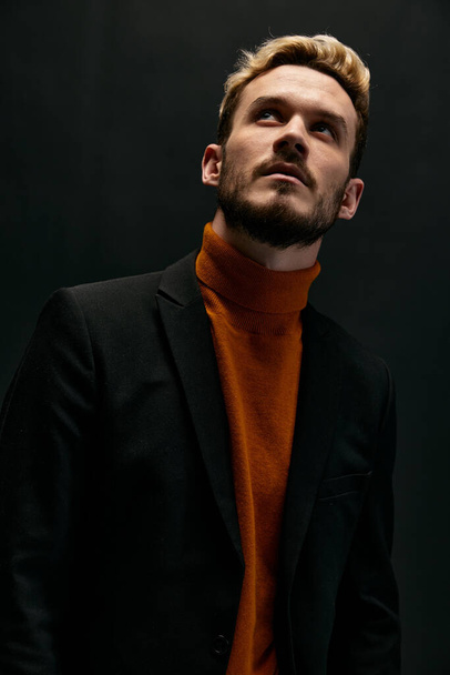 chico de moda en suéter naranja y chaqueta mirando hacia arriba en el fondo oscuro vista recortada - Foto, imagen