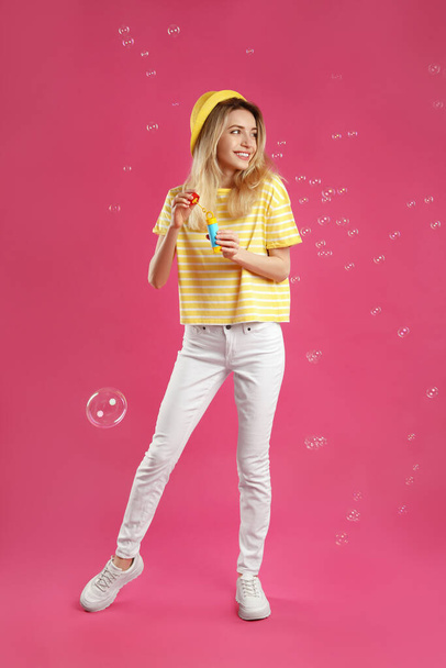 Young woman blowing soap bubbles on pink background - Fotoğraf, Görsel