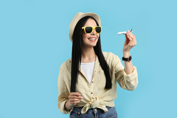 Happy female tourist with toy plane on light blue background - Foto, imagen