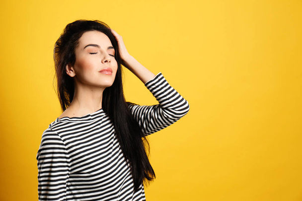 Portrait of young woman with beautiful black hair on yellow background, space for text - Фото, изображение
