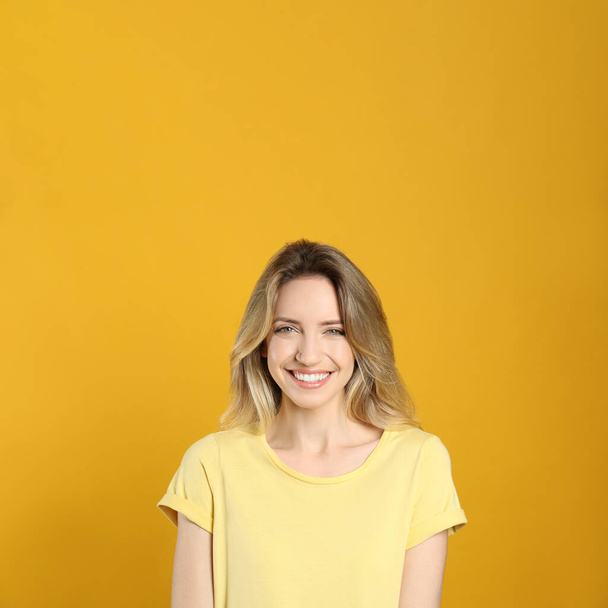 Portrait of happy young woman with beautiful blonde hair and charming smile on yellow background - Foto, immagini