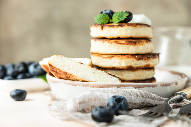 Fried cottage cheese pancakes or fritters with fresh blueberry and sour cream on a plate. Gluten free. Traditional breakfast of Ukrainian and Russian cuisine. - Foto, Imagen