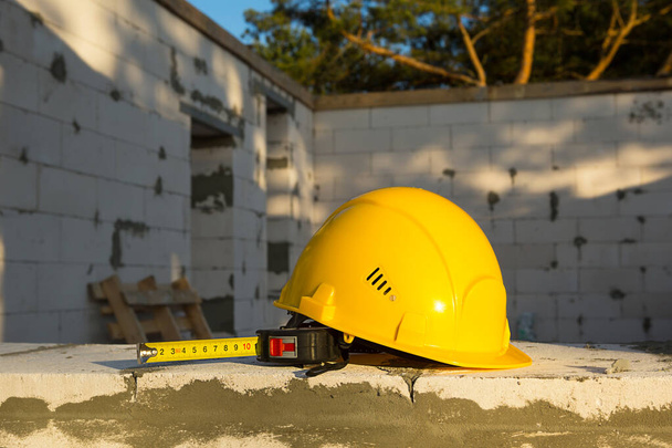 Construction hardhat and measuring tape measure on the window of a house under construction made of blocks of porous concrete. Workflow, architecture and engineering, building. Work safety and tools.  - Photo, Image