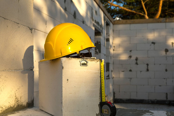 Construction yellow hardhat, key and a tape measure to house on window of housing made of blocks of porous concrete. Turnkey construction, future home, engineering, building. Work safety. Copy space - Foto, immagini