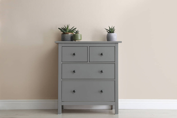 Grey chest of drawers with houseplants near beige wall - Foto, Bild