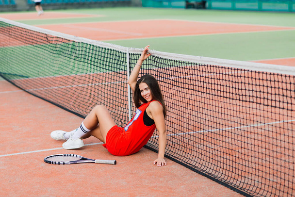 Mooie vrouwelijke tennisser op tennisbaan in rode jurk. - Foto, afbeelding