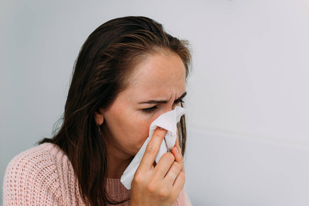 Μια λευκή γυναίκα είναι άρρωστη με κρύωμα και φυσάει τη μύτη της σε ένα μαντήλι.. - Φωτογραφία, εικόνα