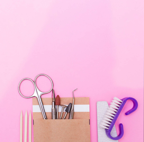 A set of cosmetics for manicure and pedicure on a pink and purple background. Gel varnishes, nail files, nail scissors, pusher, spacers and wire cutters top view. Composition for a postcard with a place for the text - Fotoğraf, Görsel