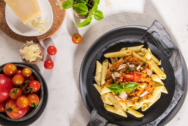 Lekker smakelijke klassieke Italiaanse penne pasta met vegetarische linzensaus, kaas parmezaanse kaas en basilicum op bord op lichte tafel. Gezond eten concept. - Foto, afbeelding