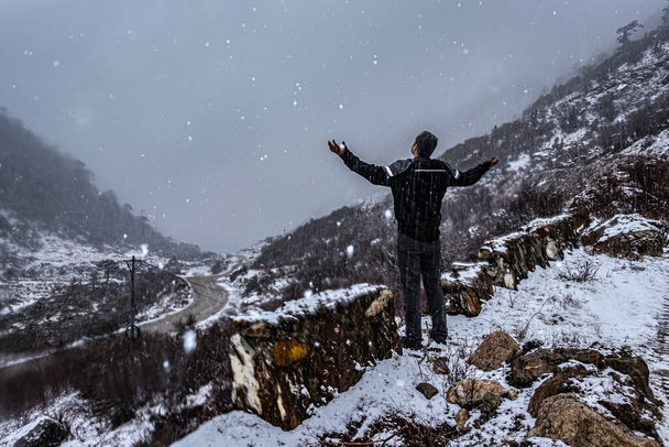 Молодой человек, наслаждающийся снегопадом в горах Гималаев на утреннем снимке снят на озере Мадури Таванг аруначал Прадеш. - Фото, изображение