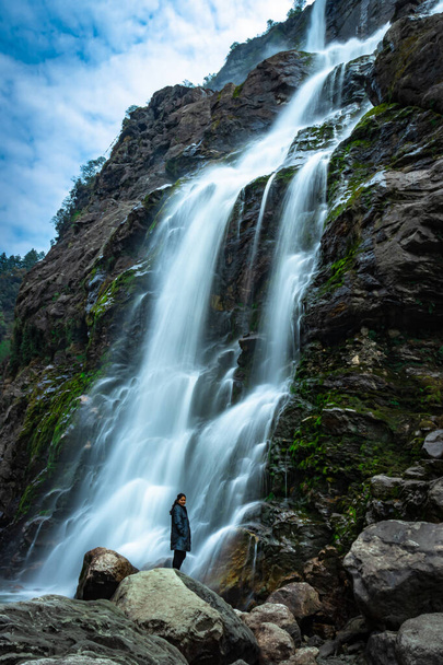 cachoeira corrente de água branca caindo de montanhas com menina de pé nas proximidades durante o dia imagem de exposição longa é tirada em jang cachoeira tawang arunachal pradesh. - Foto, Imagem