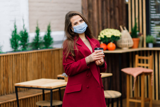 Közelkép egy orvosi maszkot viselő fehér nőről, aki az utcán és egy kávézóban áll. - Fotó, kép