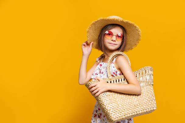 Portrait of happy cheerful girl in summer hat, sunglasses, straw bag over yellow background.  - Fotografie, Obrázek