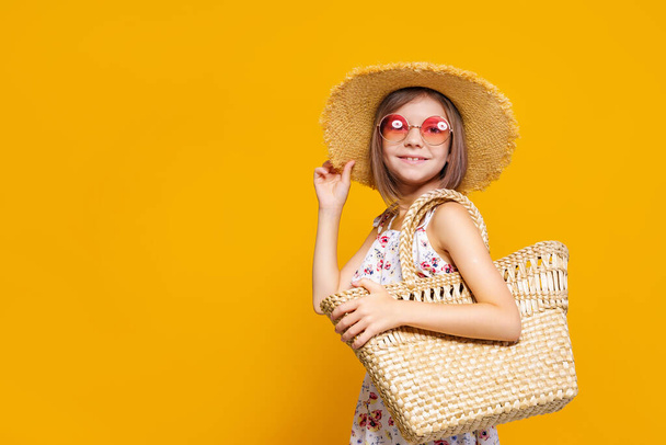 Portrait of happy cheerful girl in summer hat, sunglasses, straw bag over yellow background.  - Foto, Imagem