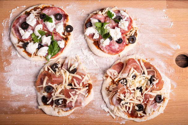 Cztery mini pizze na drewnianej desce z mąką przed pieczeniem, włoska przystawka - widok z góry - Zdjęcie, obraz