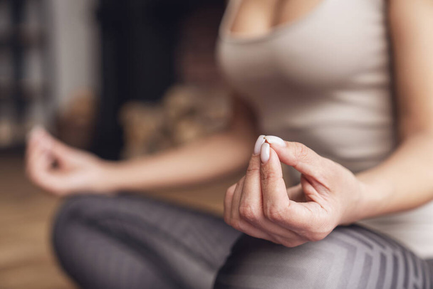 Junge schöne Fitness-Frau zu Hause sitzt in Lotusposition auf Matte während des Yoga-Kurses im Wohnzimmer zu Hause. Nahaufnahme an den Händen. - Foto, Bild