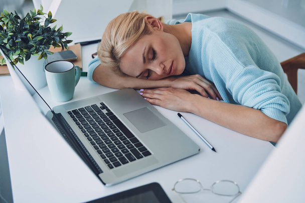 Top view of tired young woman sleeping while sitting at her working place in office - Foto, Bild