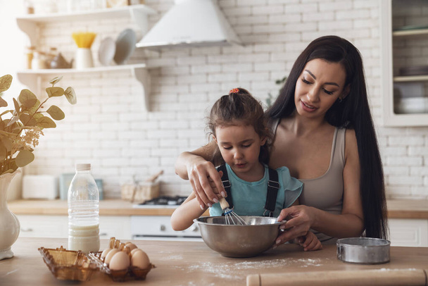 Boldog fiatal anya és kisbaba lány elkészíti a tésztát, és érezd jól magad, miközben sütit készítesz otthon a konyhában.. - Fotó, kép