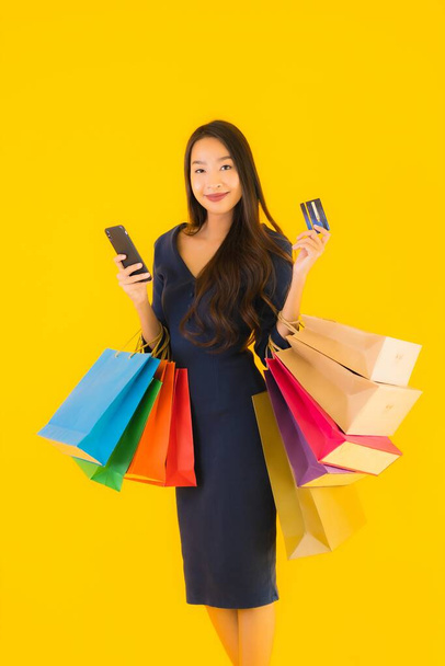 Retrato bela jovem mulher asiática com saco de compras cartão de crédito e telefone celular inteligente amarelo isolado fundo
 - Foto, Imagem