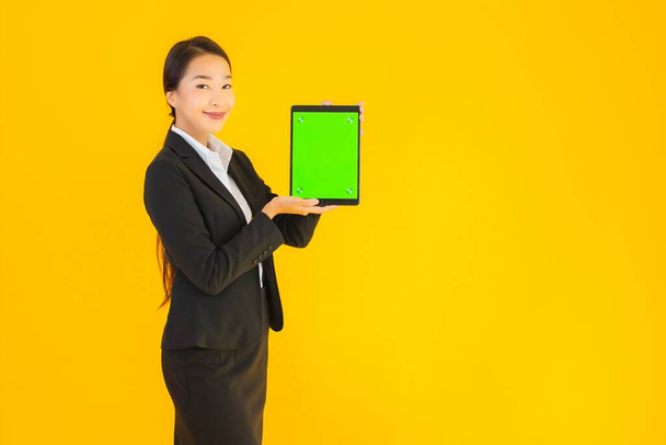Güzel, genç Asyalı bir kadının portresi mutlu bir gülümseme ve sarı izole edilmiş arka planda akıllı tabletler. - Fotoğraf, Görsel