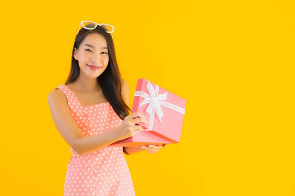 Portrét krásná mladá asijská žena s červeným dárkem box na žlutém izolovaném pozadí - Fotografie, Obrázek