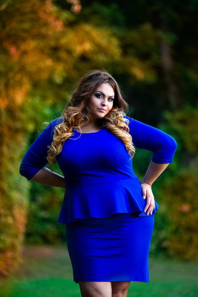 Beauty plus size model in blue dress outdoors, fat woman in autumn park among yellow leaves, beautiful hairstyle and makeup - Valokuva, kuva