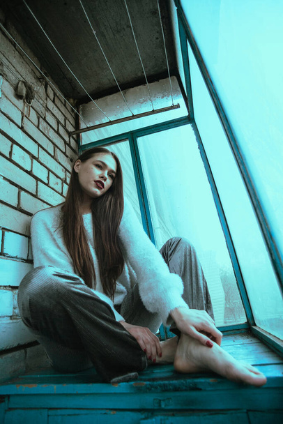 Красивая молодая сексуальная девушка позирует на балконе. Портрет девушки в современном стиле с сидячим и добавленным шумом на фото. - Фото, изображение