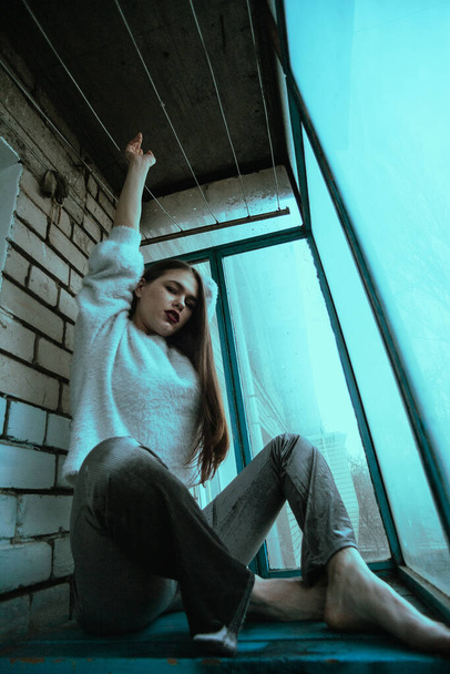 Красивая молодая сексуальная девушка позирует на балконе. Портрет девушки в современном стиле с сидячим и добавленным шумом на фото. - Фото, изображение
